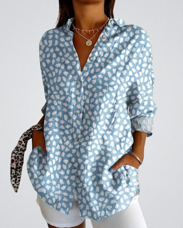Charlotte Vintage-Bluse mit weißem Blumenmuster auf hellblauem Stoff, locker geschnitten und ideal für sommerliche Outfits kombiniert mit weißen Shorts.